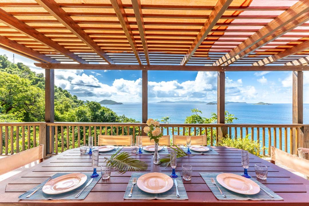 Outdoor dining table set for a meal, under a pergola with ocean views beyond