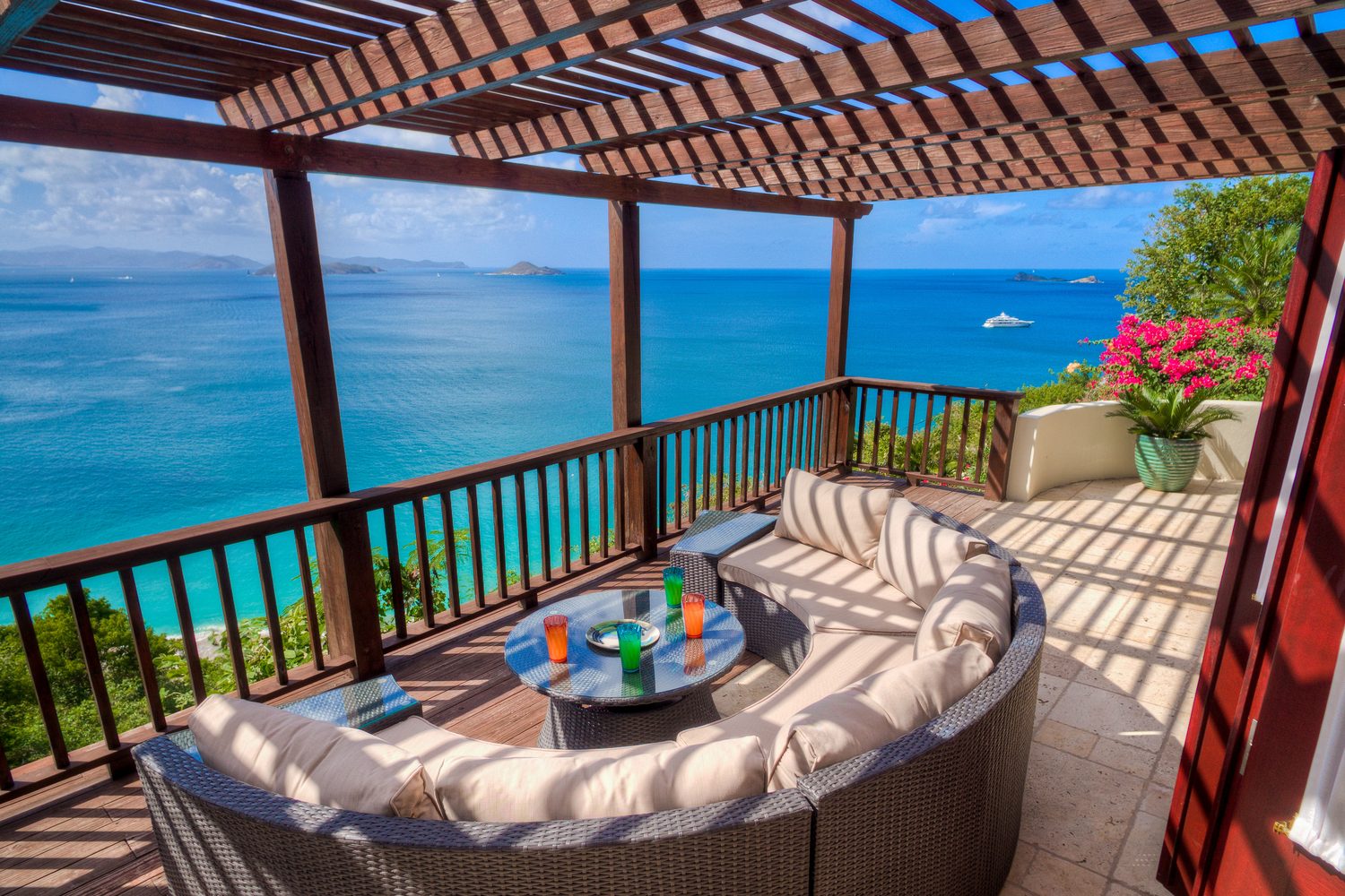 Round wicker lounge seating under the pergola, with a yacht anchored offshore