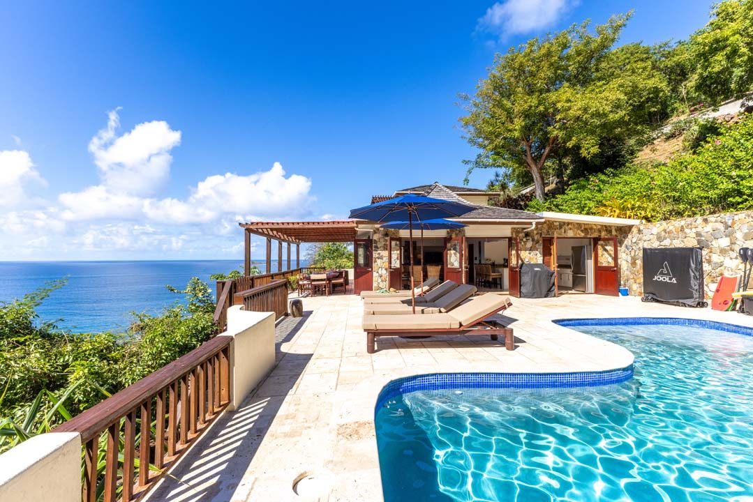 The villa's stone-edged pool and terrace, with loungers, umbrellas and open water views